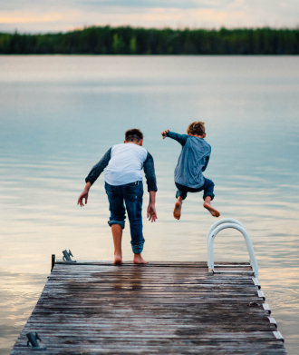 two fully clothes boys jumping off dock into lake