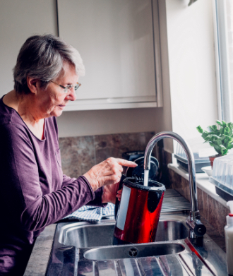 Senior woman fills a kettle with water at a sink